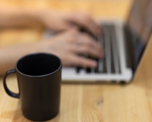 Close up of hands typing on a laptop with a coffee mug